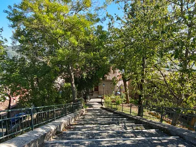 Una scalinata in sampietrini tra due ringhiere verdi, all'ombra degli alberi, con in fondo una casa e un lampione.