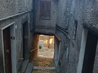 Una scalinata di sampietrini scende tra le case verso un passaggio coperto.
