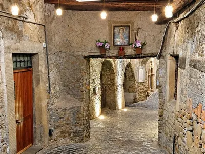 Il passaggio coperto di sera: il soffitto di travi in legno, le lampade accese e un'edicola sacra con i fiori sopra l'arco.