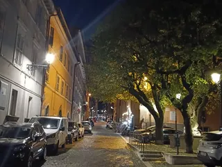 Via Borgo Mario Theodoli di sera: i sampietrini illuminati dai lampioni, le facciate dei palazzi e gli alberi sul lato della strada.