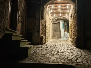 Un passaggio coperto del centro storico di sera: l'arco in pietra, il soffitto di travi in legno illuminato da piccole lampade e il selciato di sampietrini.