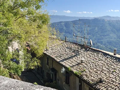 I tetti in coppi e le antenne sopra un vicolo, con la valle verde e i paesi sulle colline di fronte.