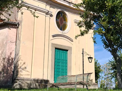 La facciata della chiesa vista dal prato, con una vecchia panchina in ferro davanti al portone.