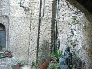 Portico ombreggiato con vasi di piante e una piccola statua.