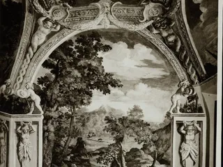 Fotografia d'archivio in bianco e nero di un affresco degli interni: un paesaggio con cacciatori e cani, incorniciato da putti, festoni e telamoni dipinti.