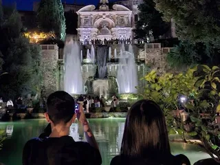 Visitatori che fotografano la Fontana dell'Organo dalle Peschiere, di sera.
