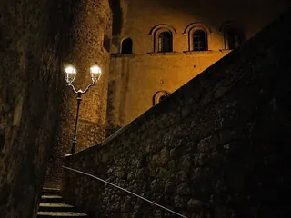 Il castello di notte, visto dalla scalinata in selciato nei pressi della Chiesa di Santa Maria de Arce: la torre rotonda e le finestre ad arco alla luce dei lampioni.
