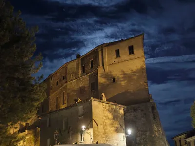Il castello di notte, illuminato dai lampioni sotto un cielo di nuvole rischiarate dalla luna.