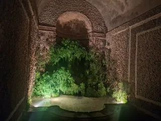 Un ninfeo in grotta con felci e una vasca d'acqua.