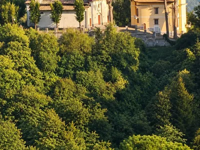 Il santuario tra i pini, in cima al colle coperto di boschi, con un borgo sullo sfondo.