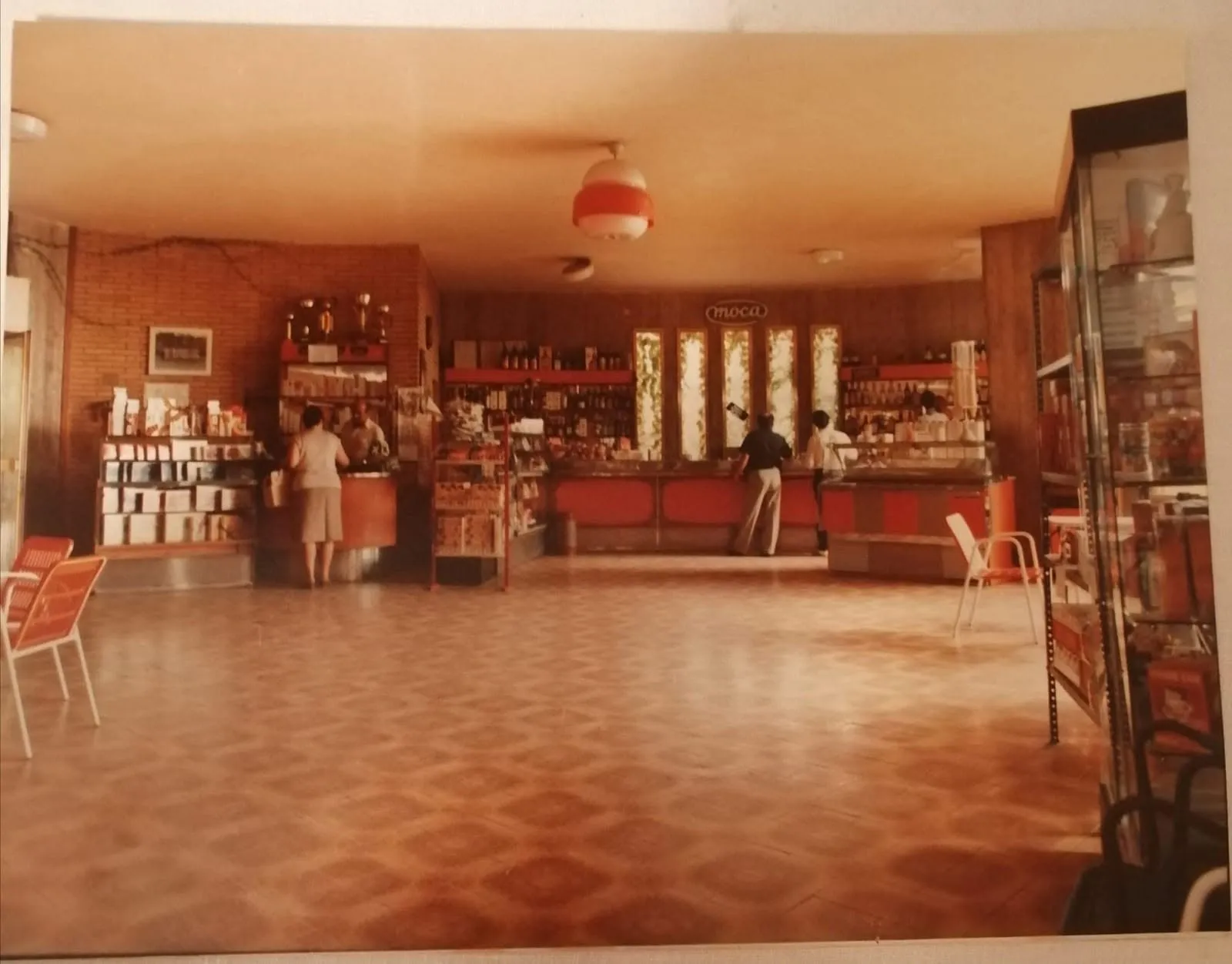 Il salone principale del bar, con i clienti al bancone e il grande lampadario al centro.