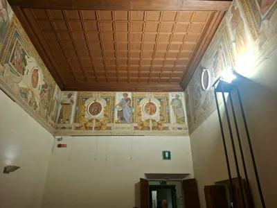 Una sala con soffitto a cassettoni in legno e un fregio di figure affrescate.