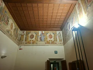 Una sala con soffitto a cassettoni in legno e un fregio di figure affrescate.